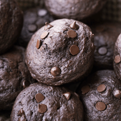 Several sourdough double chocolate chip muffins sit in a basket lined with a kitchen towel.