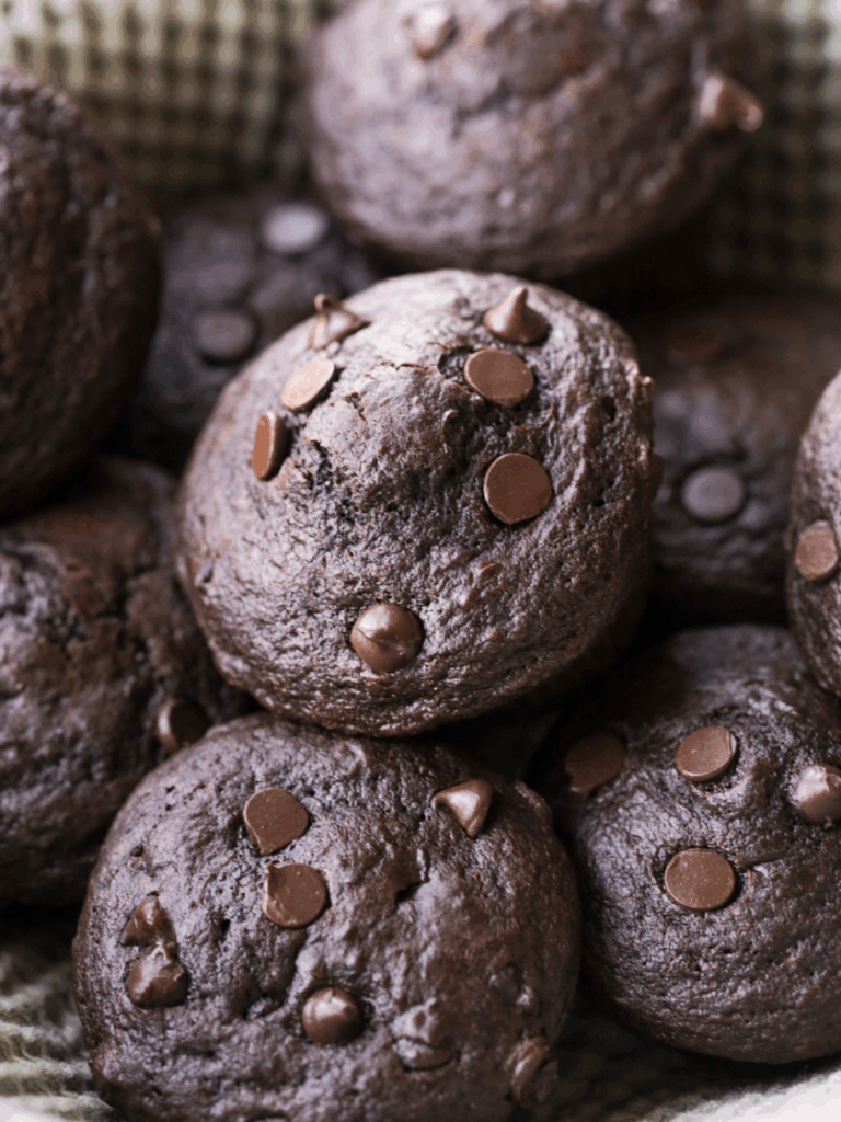 Several sourdough double chocolate chip muffins sit in a basket lined with a kitchen towel.