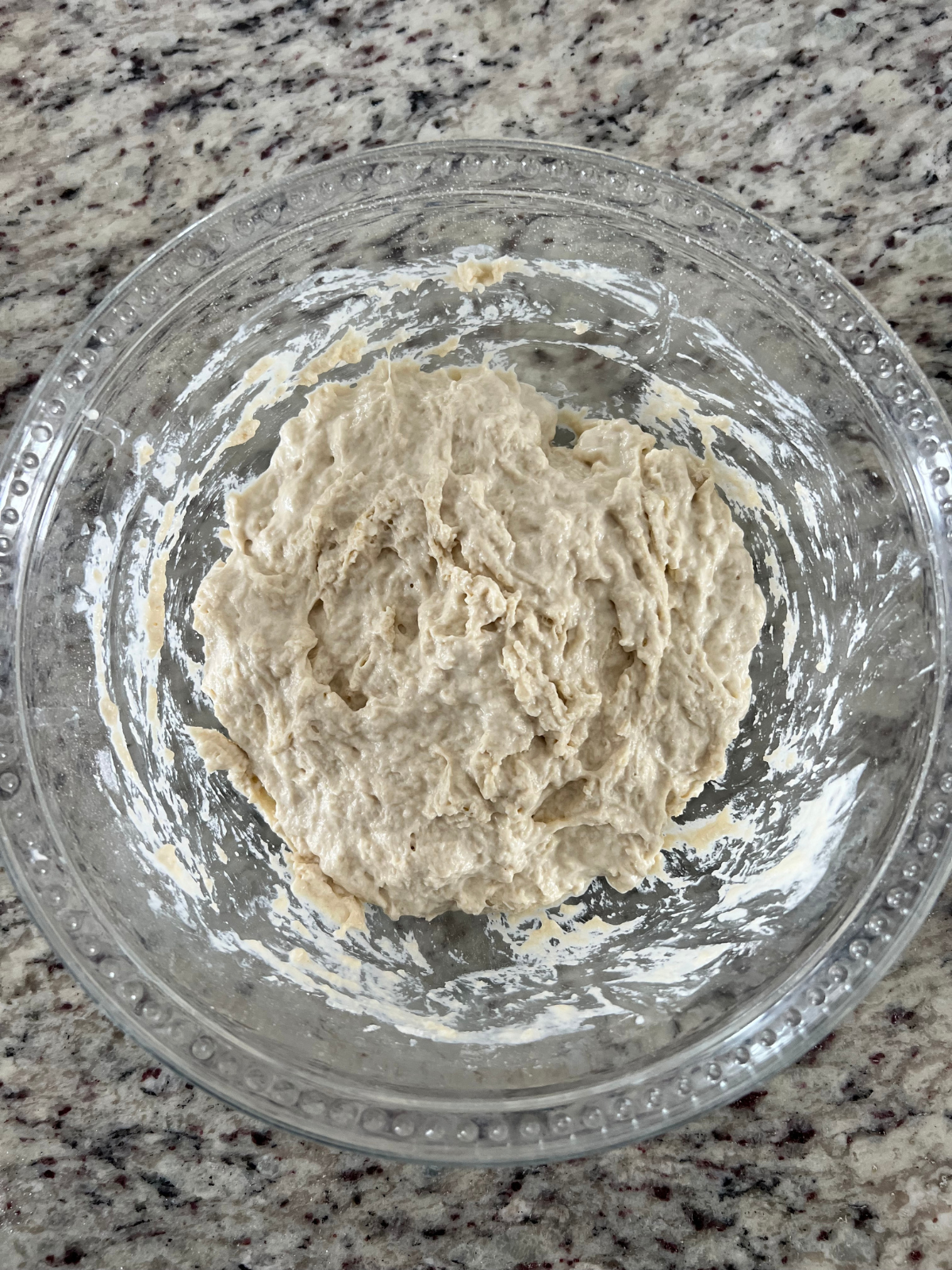 The sourdough focaccia ingredients have been mixed into a shaggy dough ball and now sit in a glass mixing bowl.