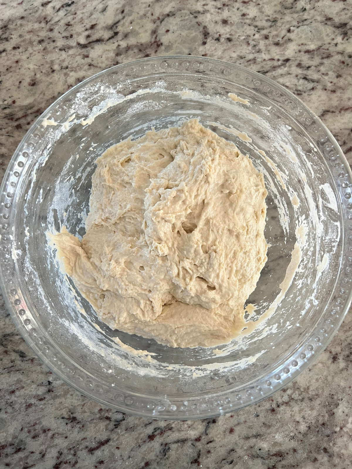 A glass mixing bowl contains the mixed sourdough fry bread dough. 