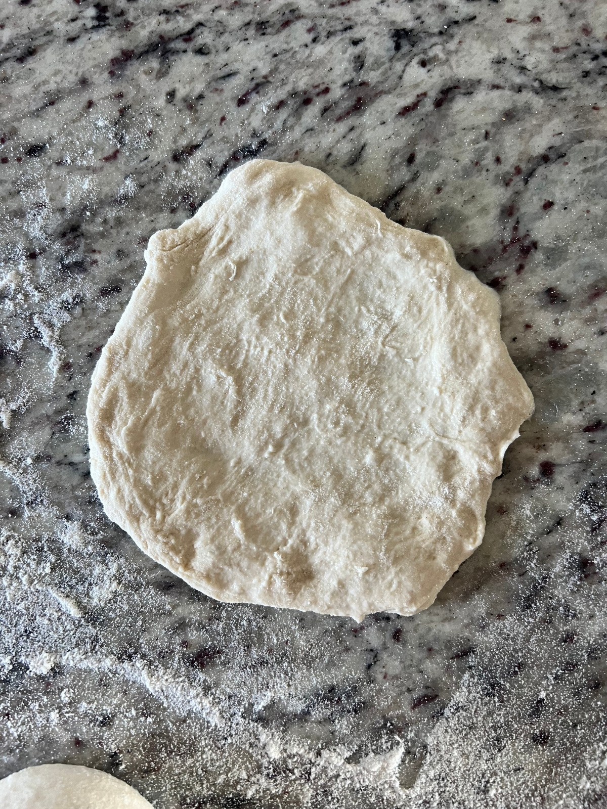 The sourdough fry bread dough ball has been flattened out into a flat, round shape.