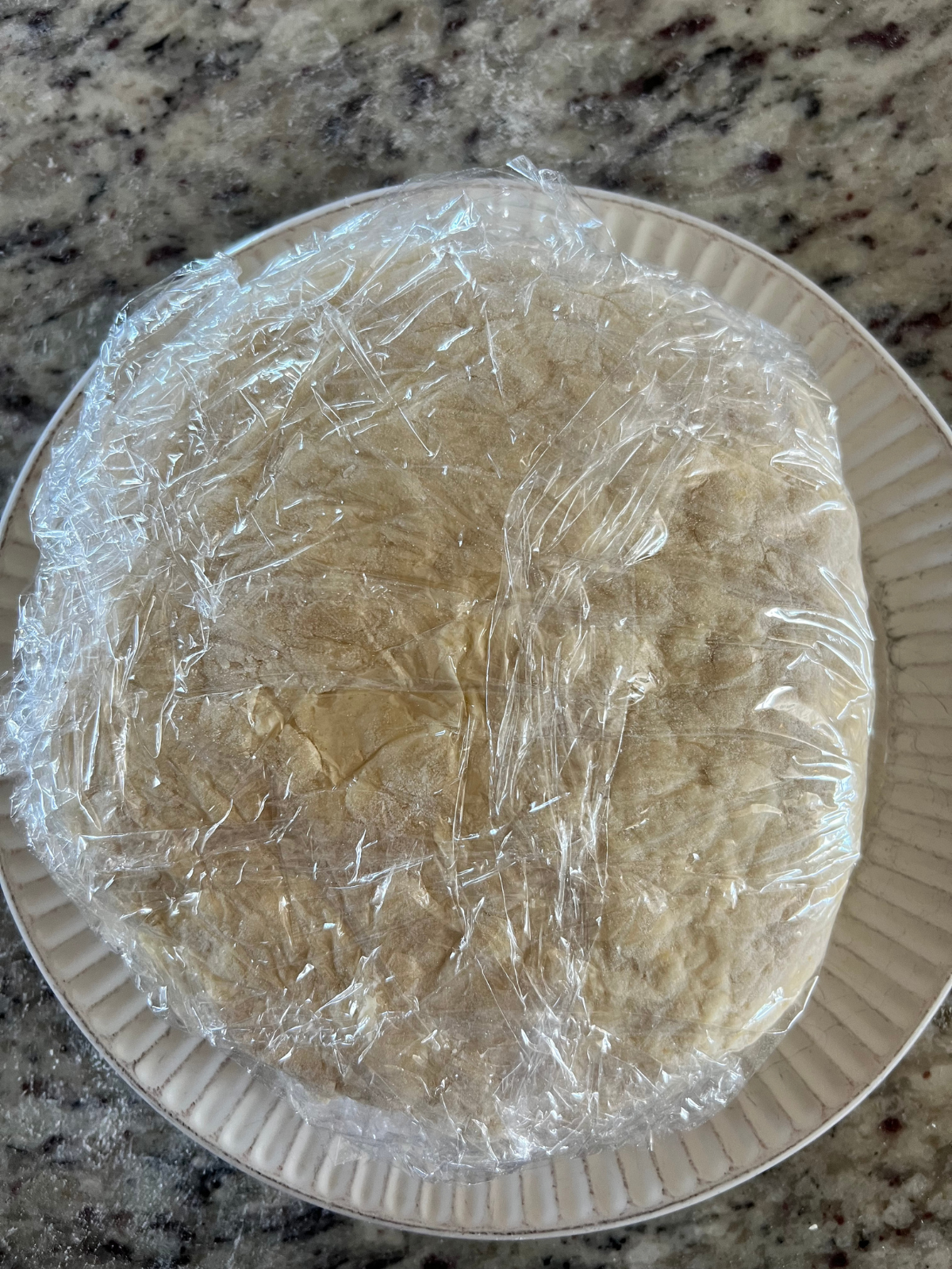The sourdough lemon scone dough disc is wrapped in plastic wrap and sits on a plate.