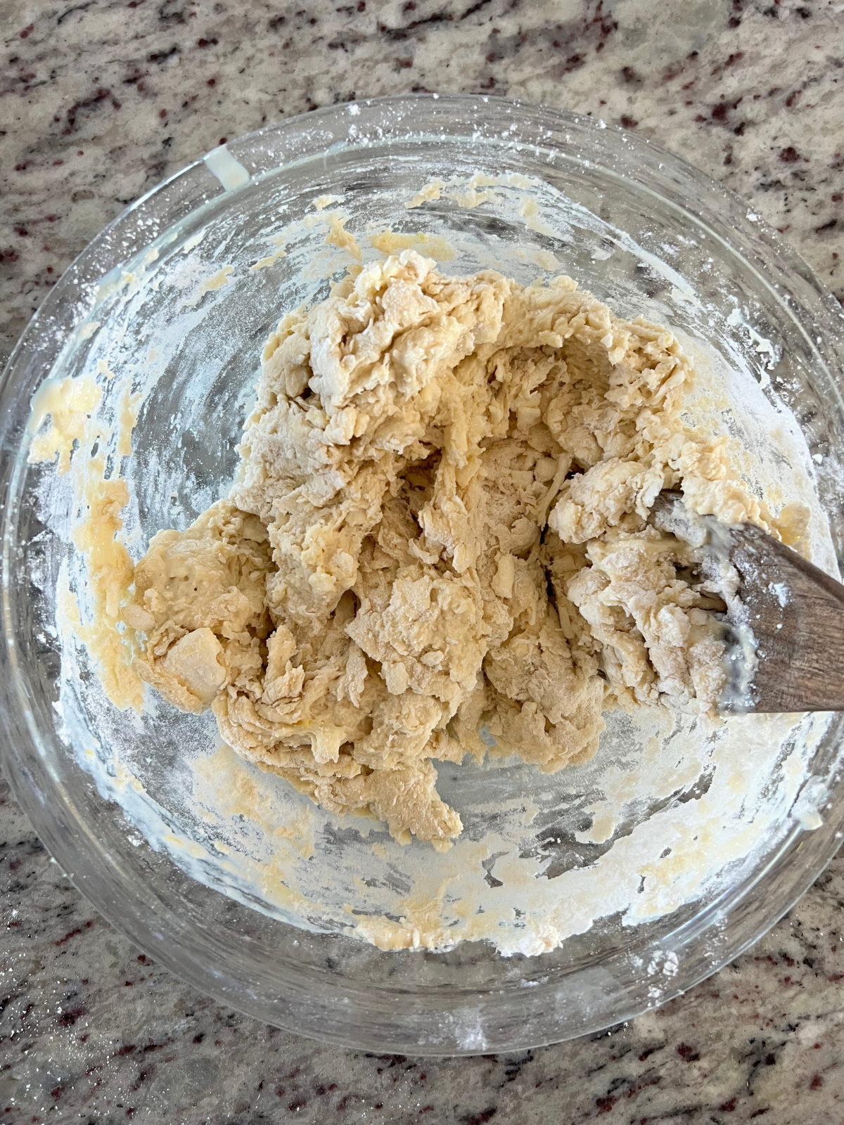 The dough has been mixed into a shaggy ball. It is shown in a mixing bowl with a wooden spoon.