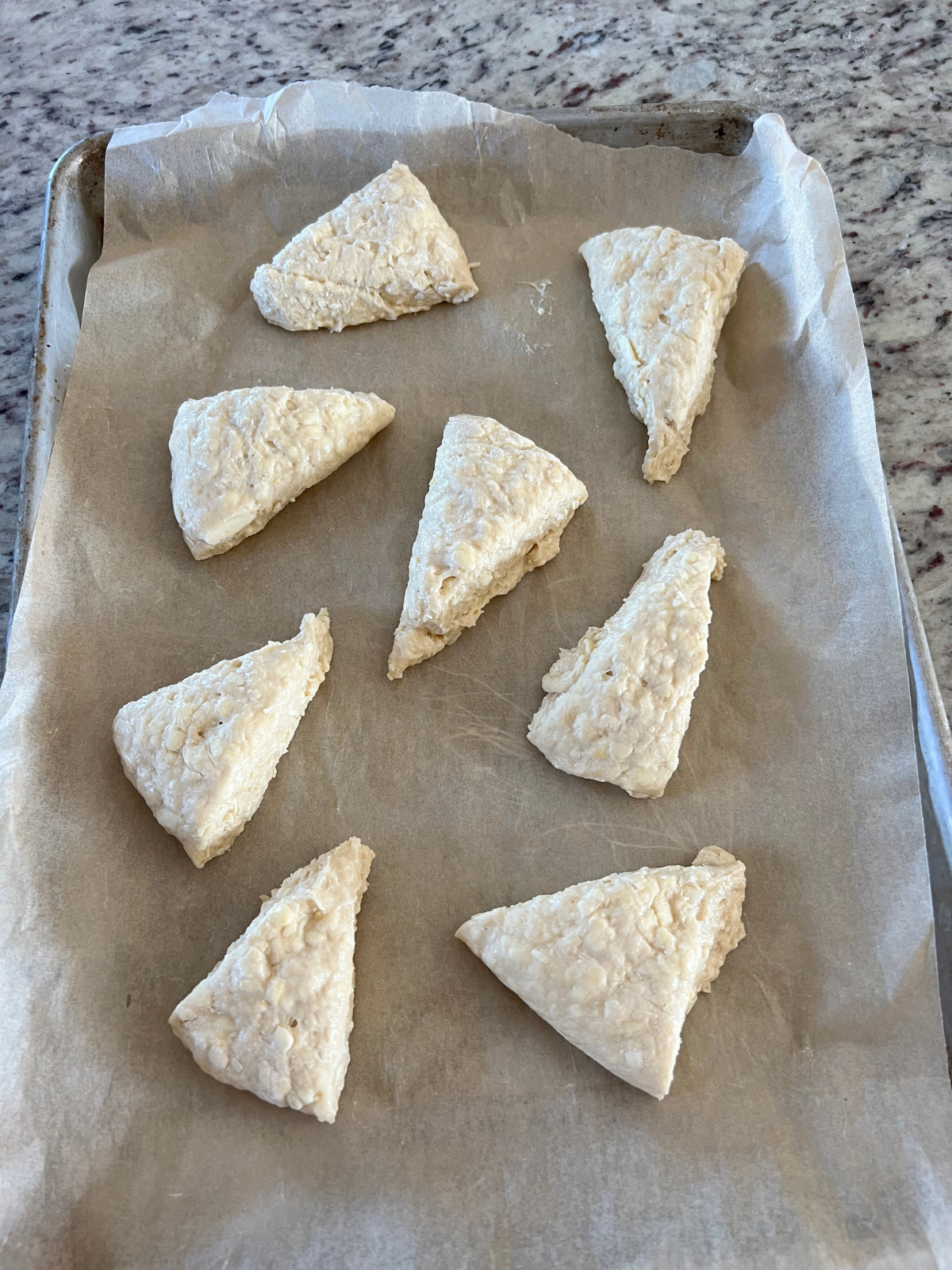 The sourdough lemon scone dough pieces sit on a parchment-lined baking sheet.