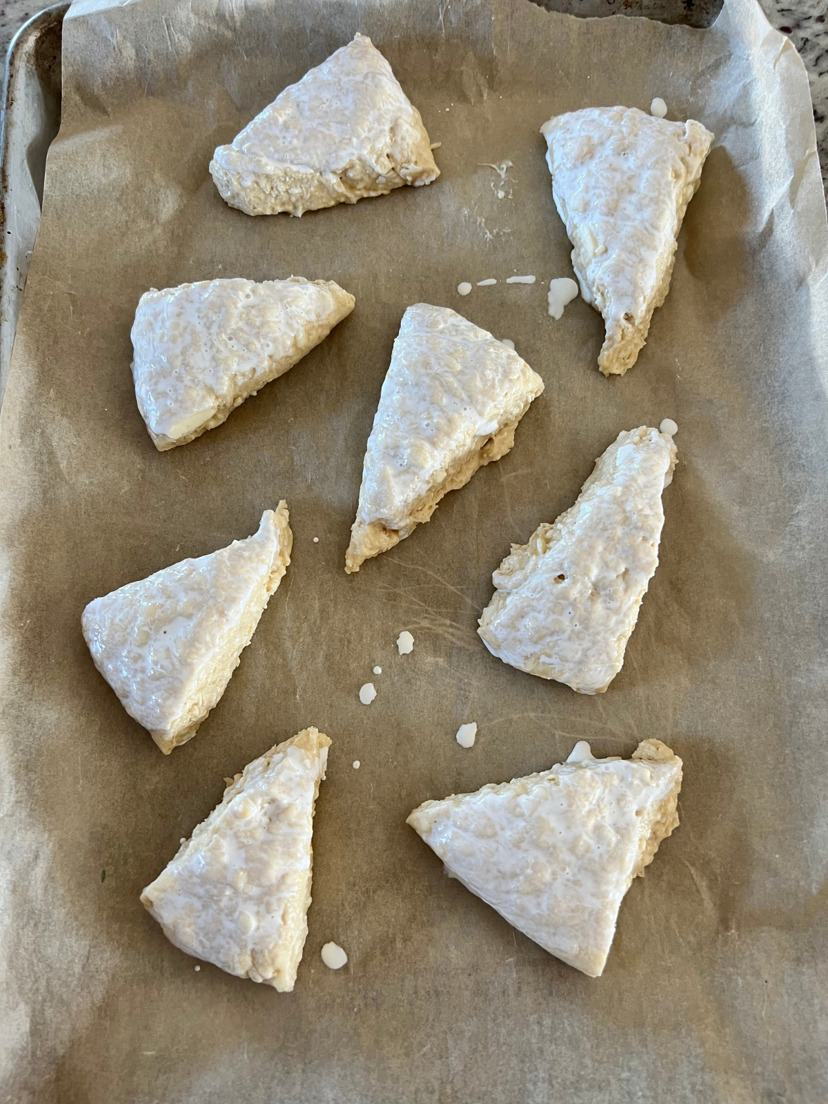 The sourdough lemon scone dough sits on a baking sheet. They are each brushed with heavy cream.