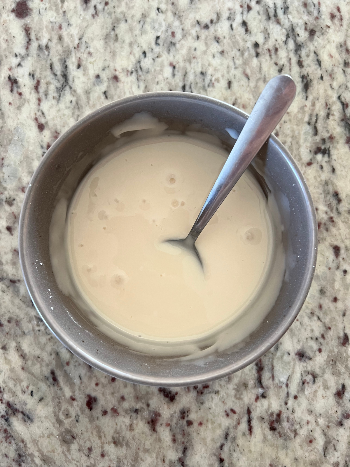 The lemon icing sits in a bowl with a spoon sitting in it.