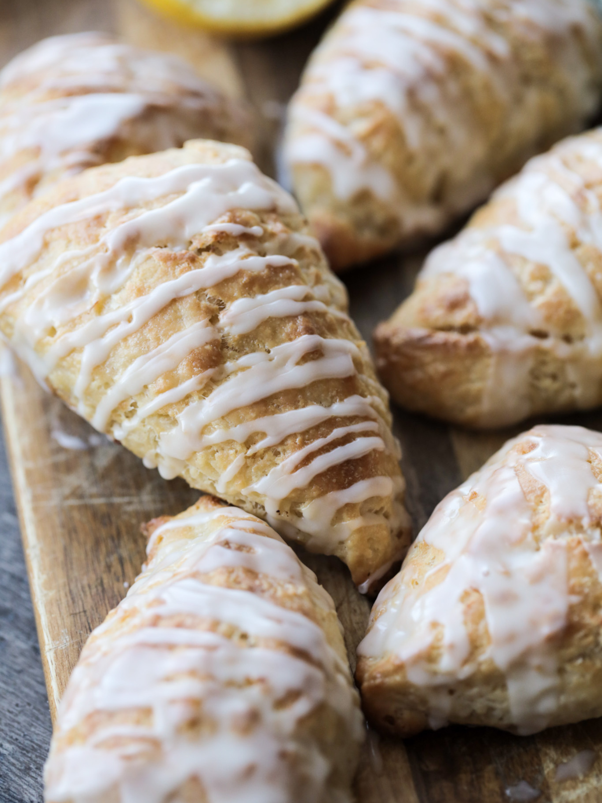 Several lemon sourdough scones with lemon glaze sit on a wooden platter.