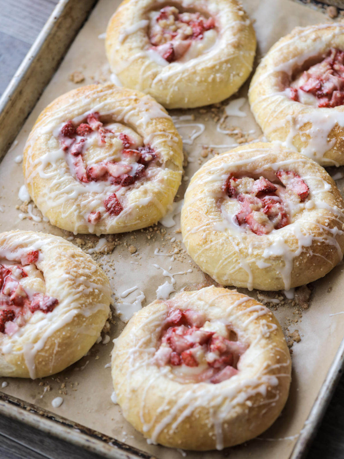 The baked sourdough strawberry cream cheese buns sit on a baking sheet. They are freshly baked and topped with icing.