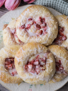 Several sourdough discard strawberry cream cheese buns sitting on a floral plate. They are covered in streusel and icing.