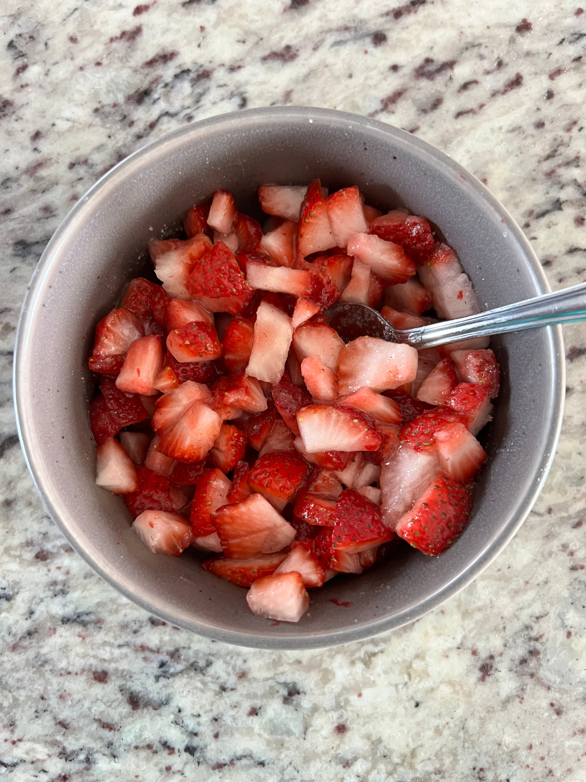 Two cups of diced strawberries sit in a bowl with sugar. They will rest in the fridge to be macerated before topping the sourdough sweet buns.
