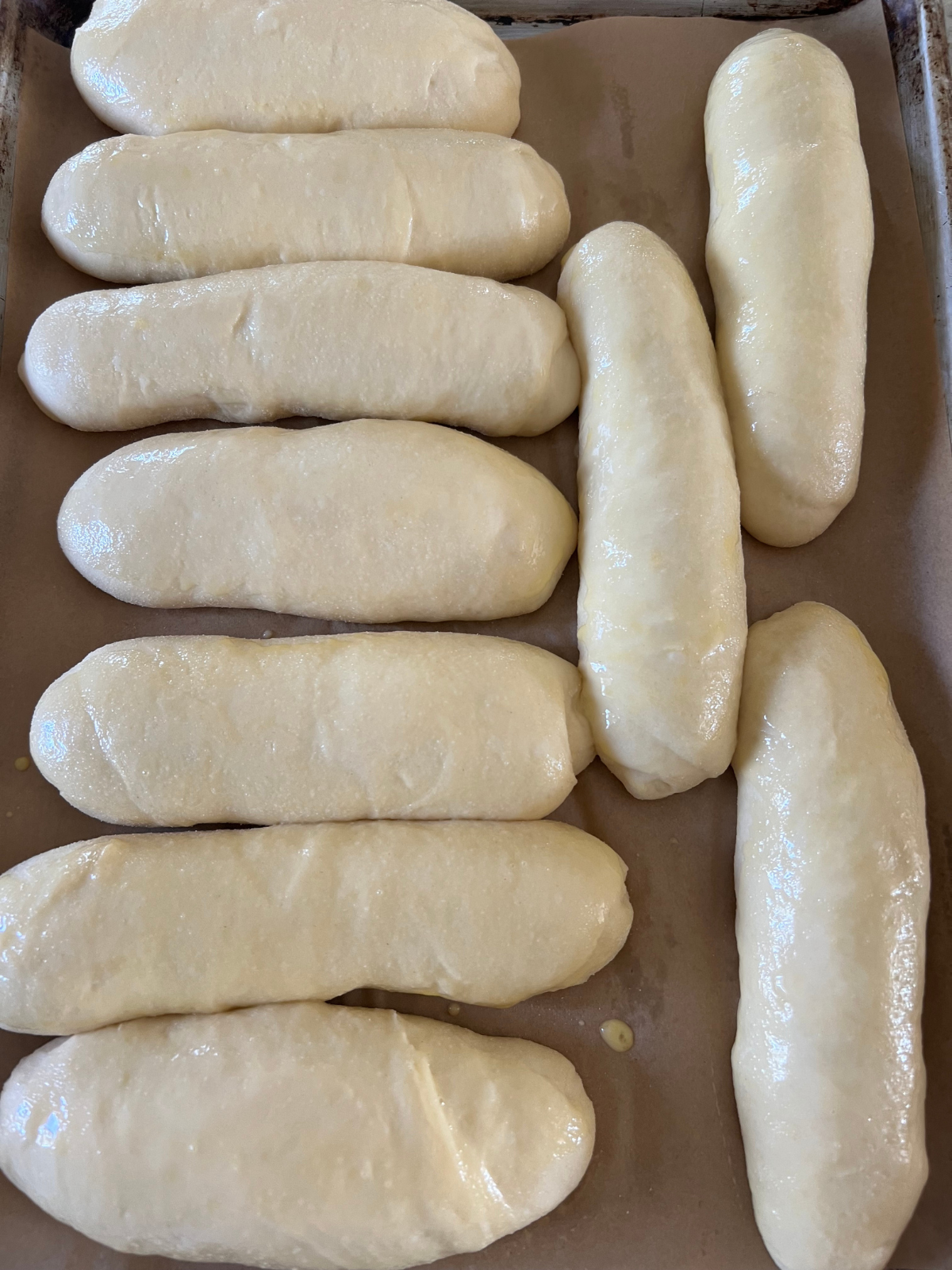 The sourdough hot dog buns have risen and are ready to bake. The egg wash has been brushed over them. 