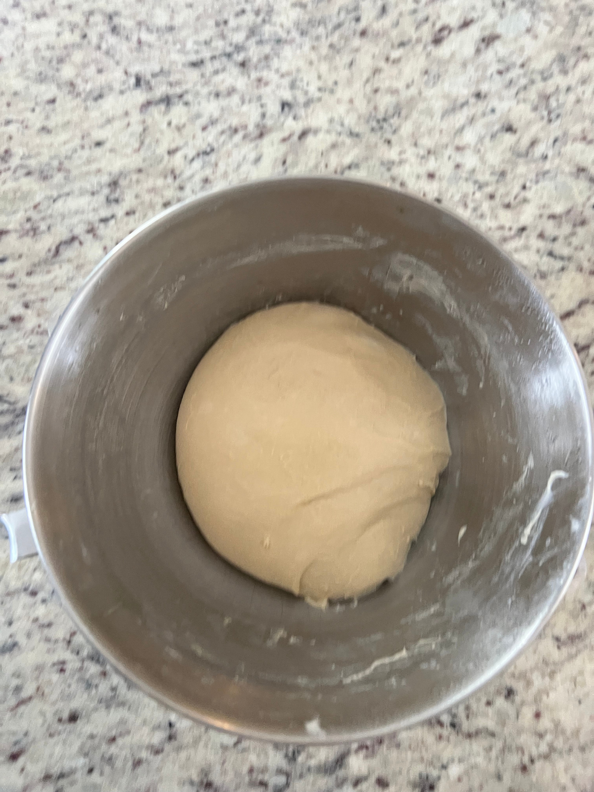 Sourdough brioche bun dough sits in the bowl of a stand mixer after being kneaded.