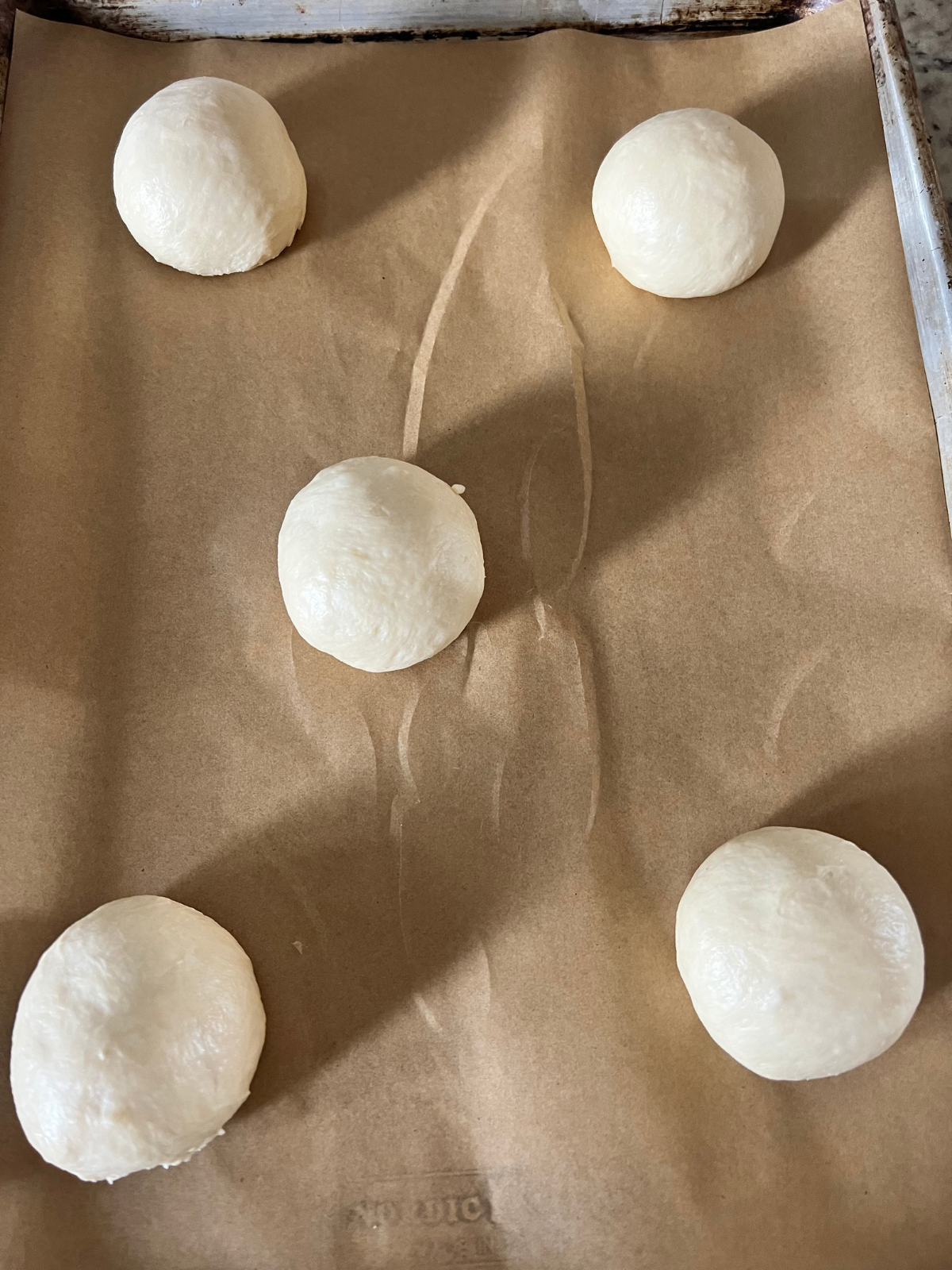 The sourdough brioche burger bun dough balls are resting on a parchment paper-lined baking sheet preparing for their second rise.