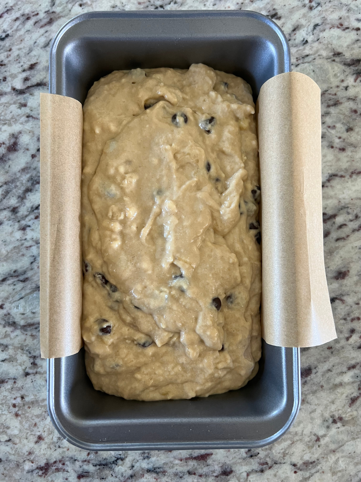 The sourdough brown butter banana bread batter sits in a parchment paper-lined loaf pan.