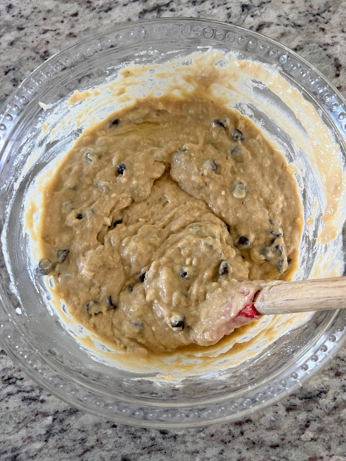The sourdough brown butter banana bread batter sits in a glass mixing bowl with a rubber spatula in it.