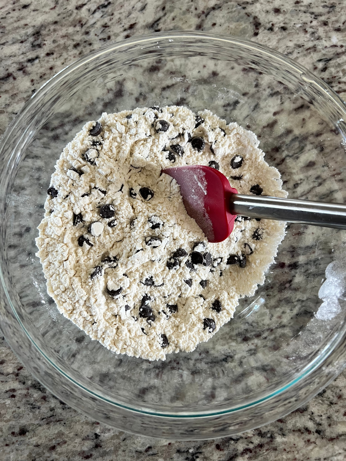 The dry ingredients, along with the chocolate chips, sit in a glass mixing bowl. 