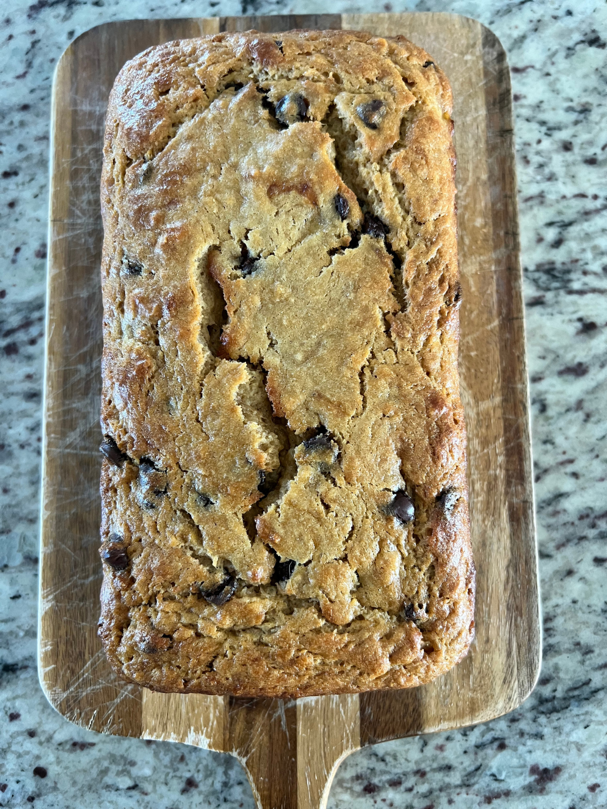 The freshly baked sourdough brown butter banana bread sits on a wooden cutting board, cooling.
