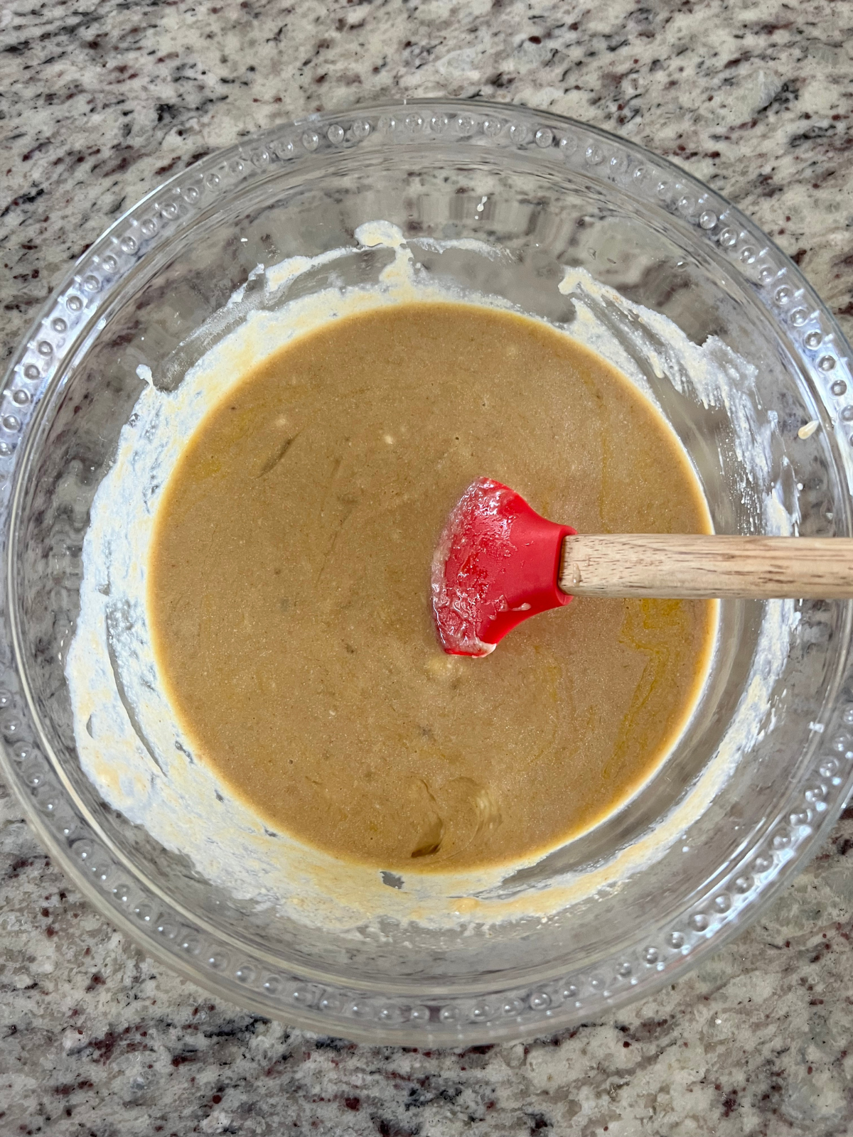 The wet ingredients for the sourdough brown butter banana bread sit in a glass mixing bowl with a rubber spatula in it.
