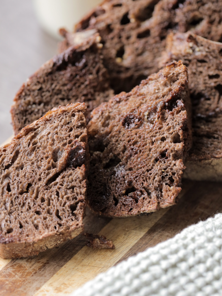 Several slices of sourdough chocolate coffee bread sit on a wooden cutting board.