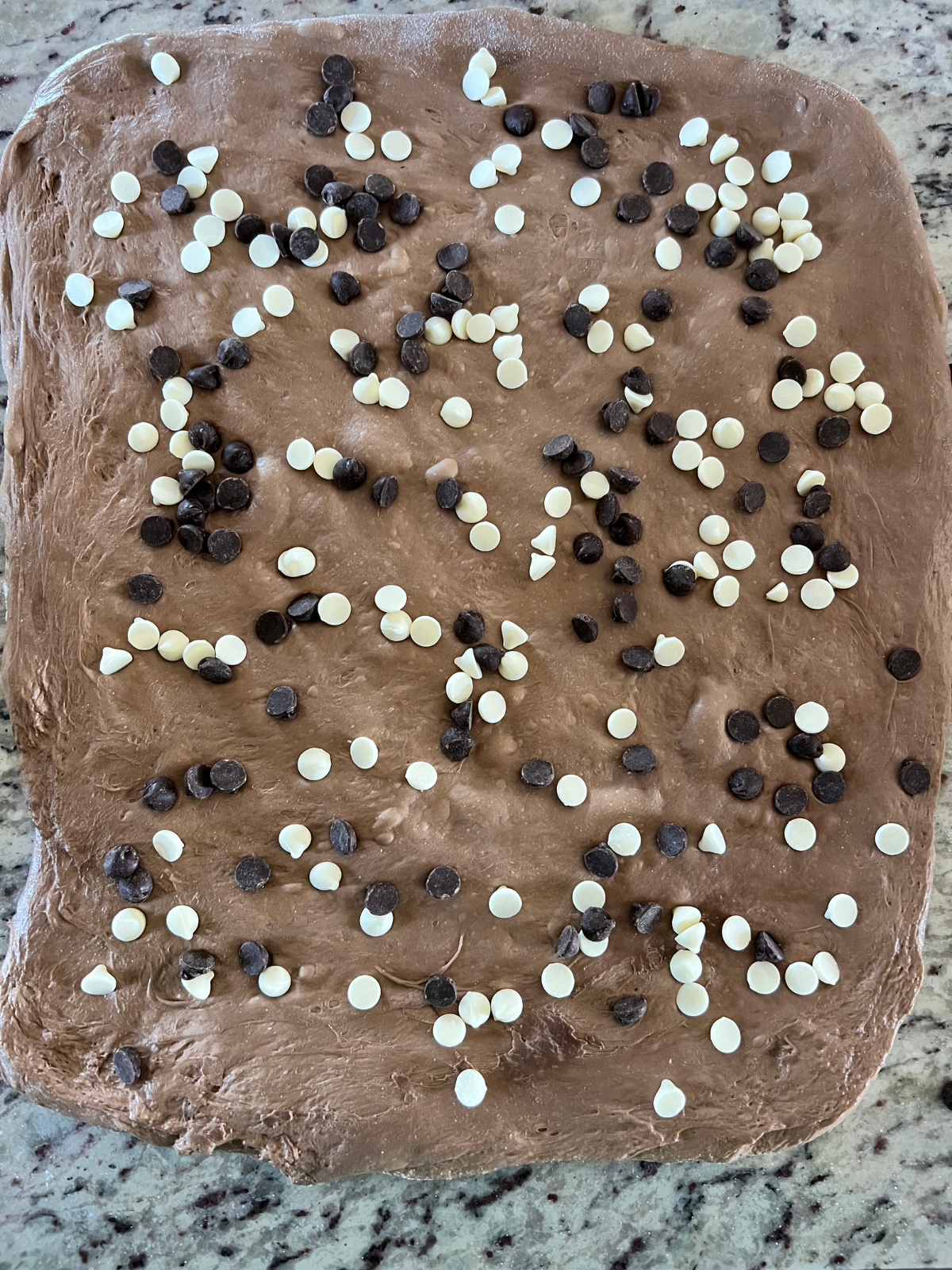 The dough is stretched out into a rectangle with white chocolate chips and semi-sweet chocolate chips sprinkled evenly over it.