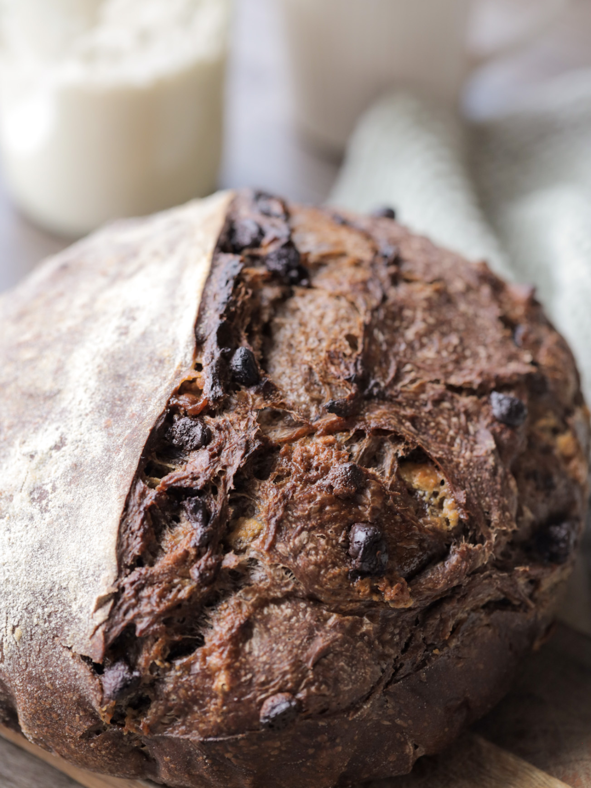 A whole sourdough chocolate and white chocolate coffee bread loaf rests on a wooden cutting board.