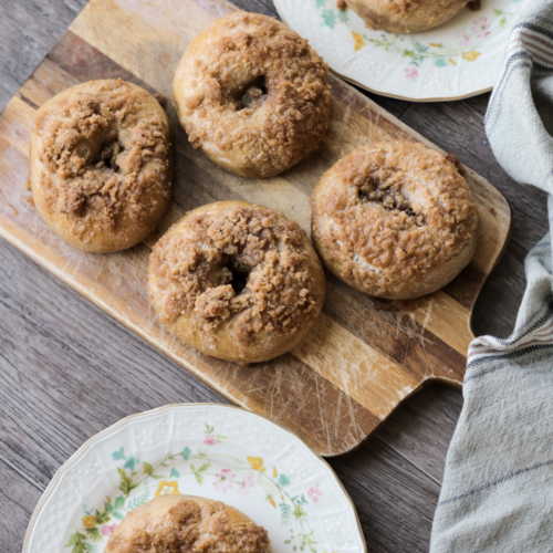 Sourdough cinnamon crunch bagels rest on two floral plates and also on a wooden cutting board.