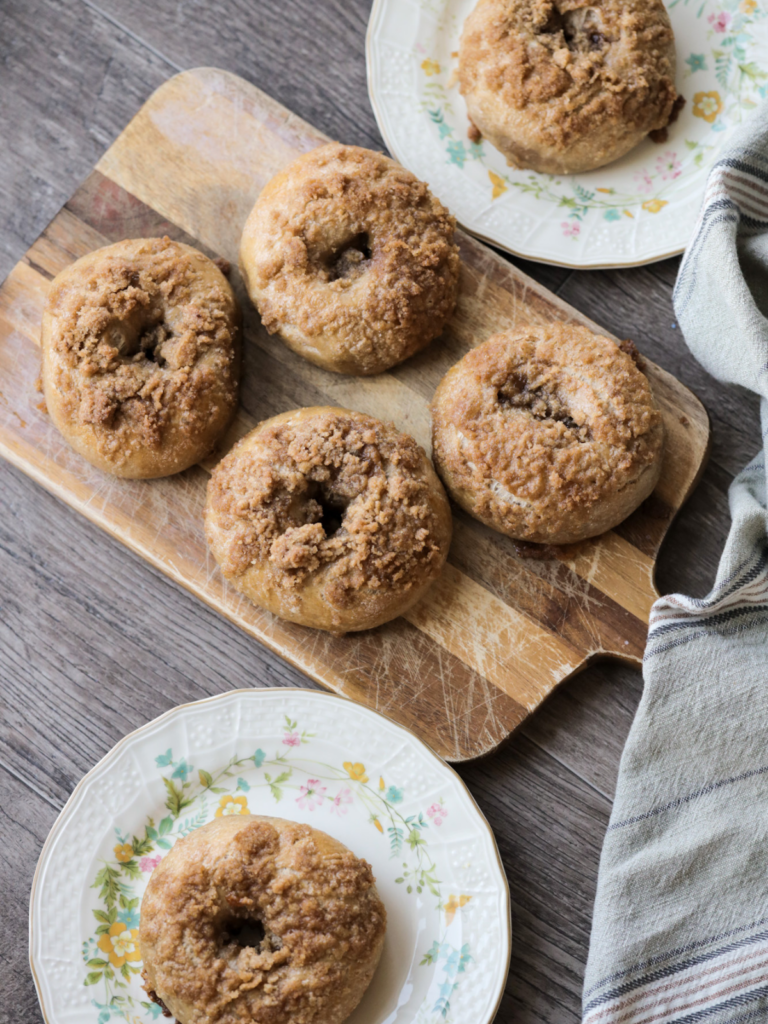 Sourdough cinnamon crunch bagels rest on two floral plates and also on a wooden cutting board.