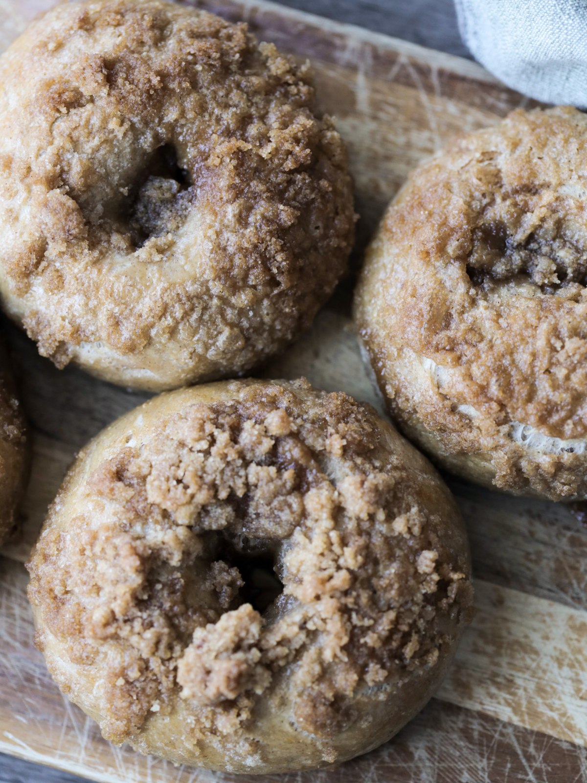 Three sourdough cinnamon crunch bagels rest on a wooden cutting board.