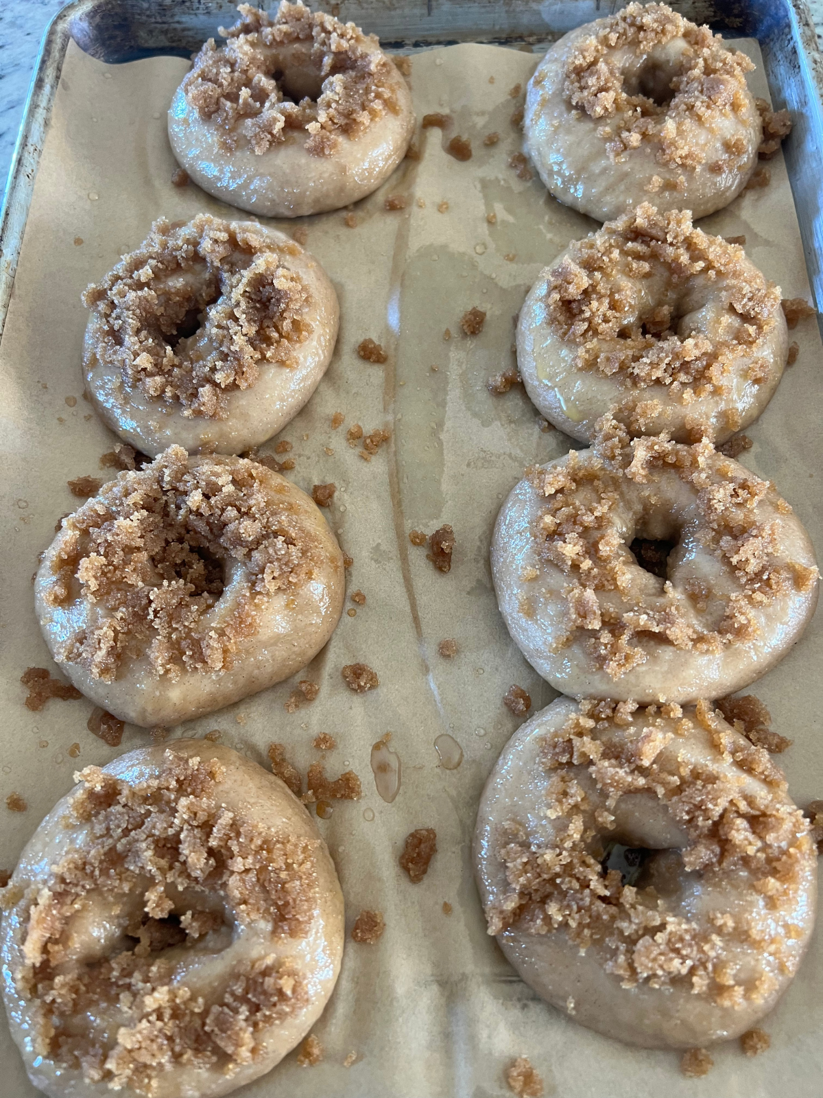 The sourdough cinnamon crunch bagels are topped with the crumble and are sitting on a parchment paper lined baking sheet preparing to bake.
