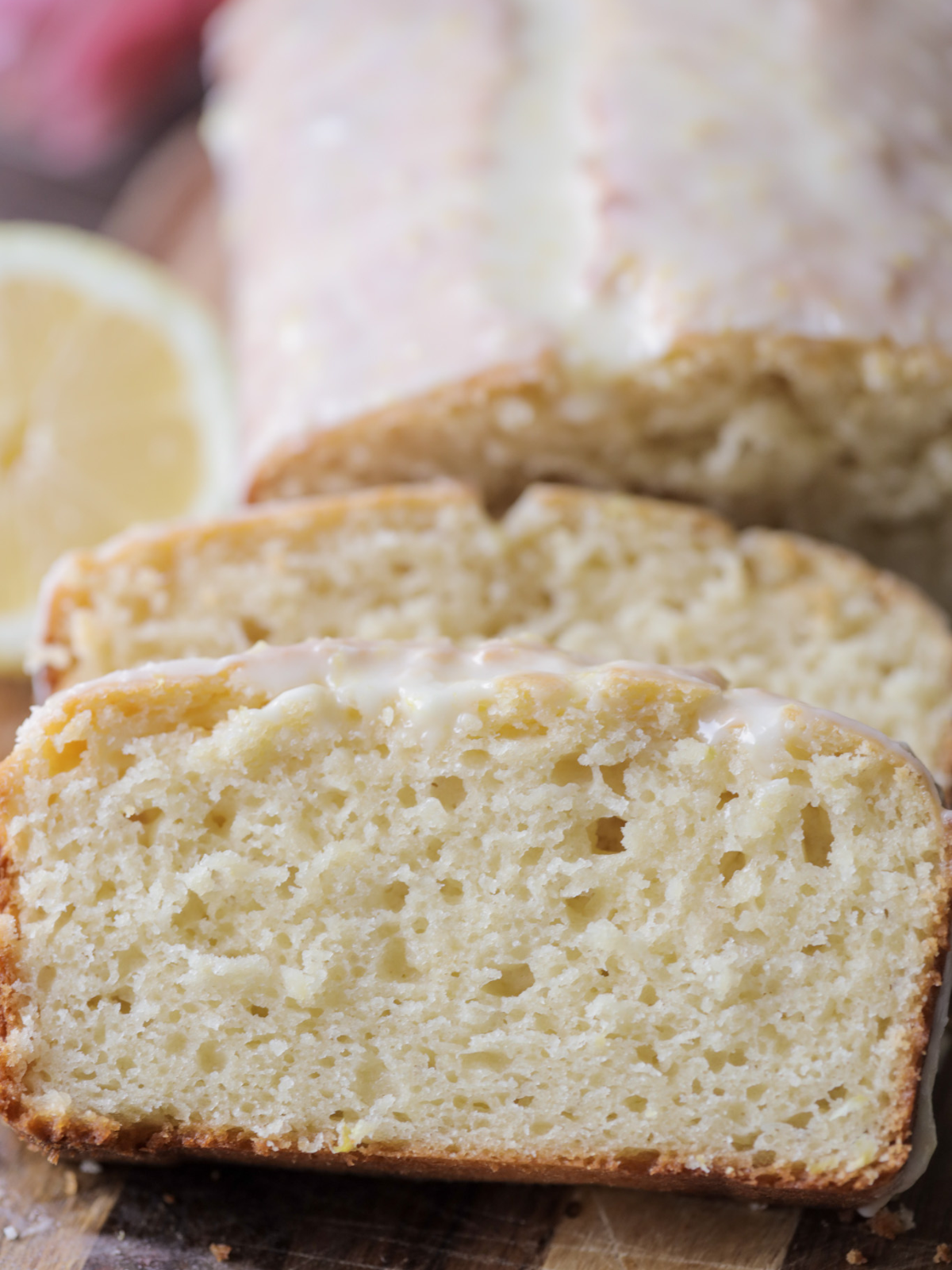 Sourdough lemon pound cake with a lemon glaze sits behind two big slices of the cake.
