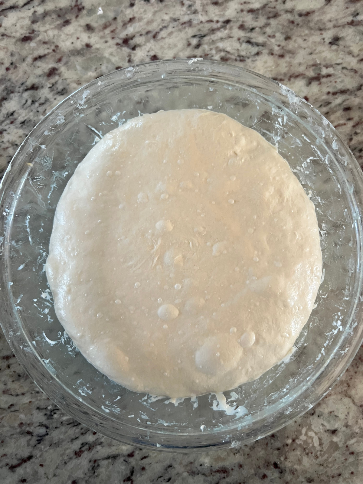 The sourdough pickle focaccia dough is shown in a glass bowl after several stretch and folds and bulk fermentation completed.