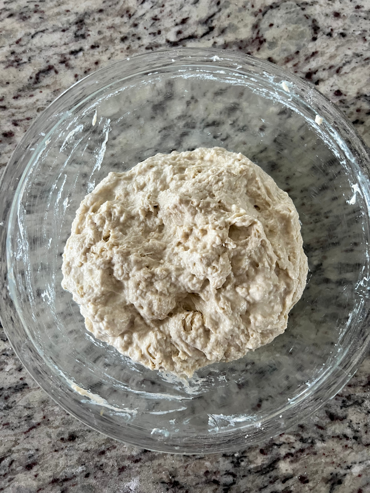 The sourdough pickle focaccia dough has just been mixed together in a shaggy dough. It sits in a glass mixing bowl.