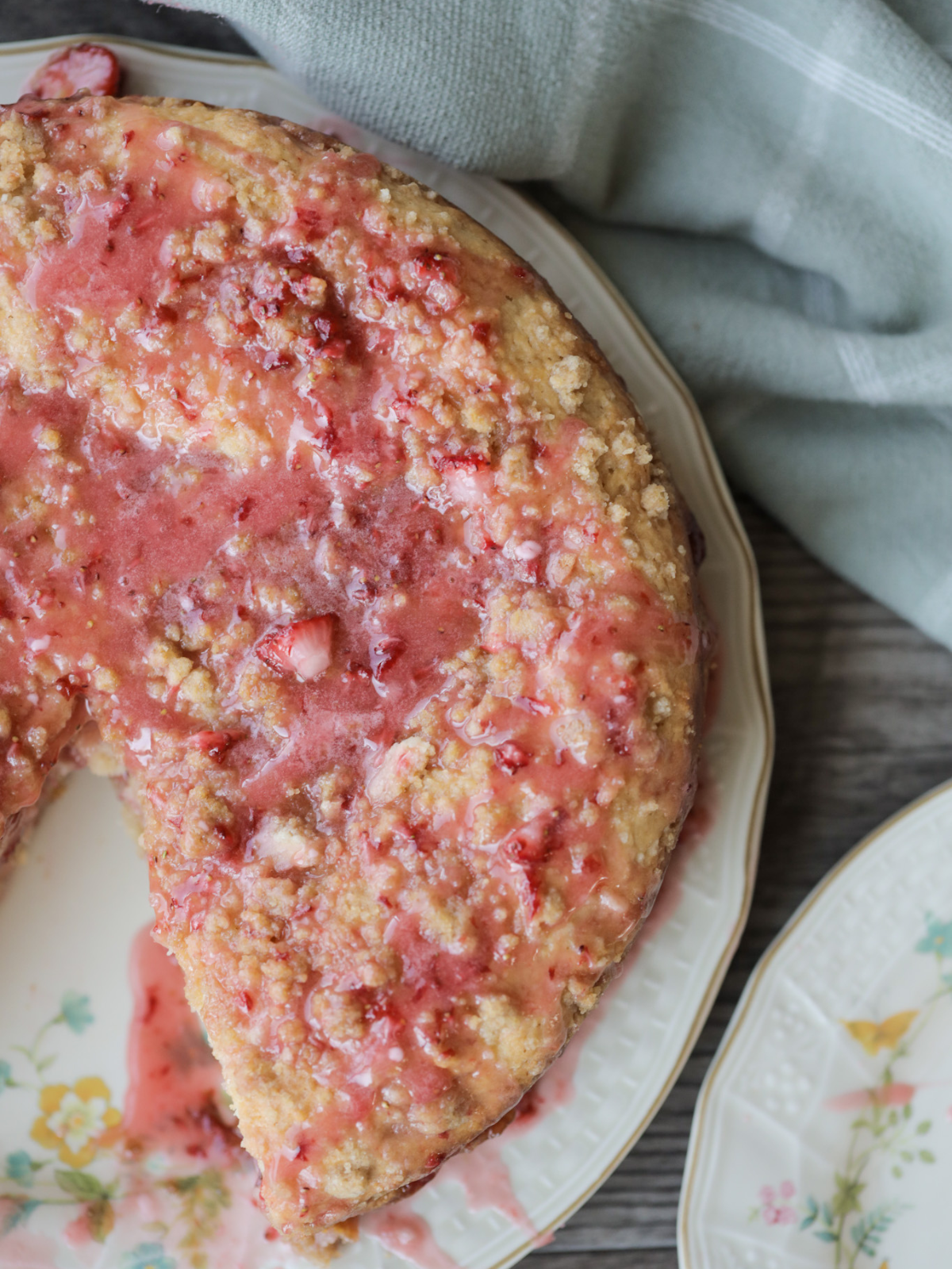 Half of the sourdough strawberry coffee cake with strawberry icing sits on a floral plate. 
