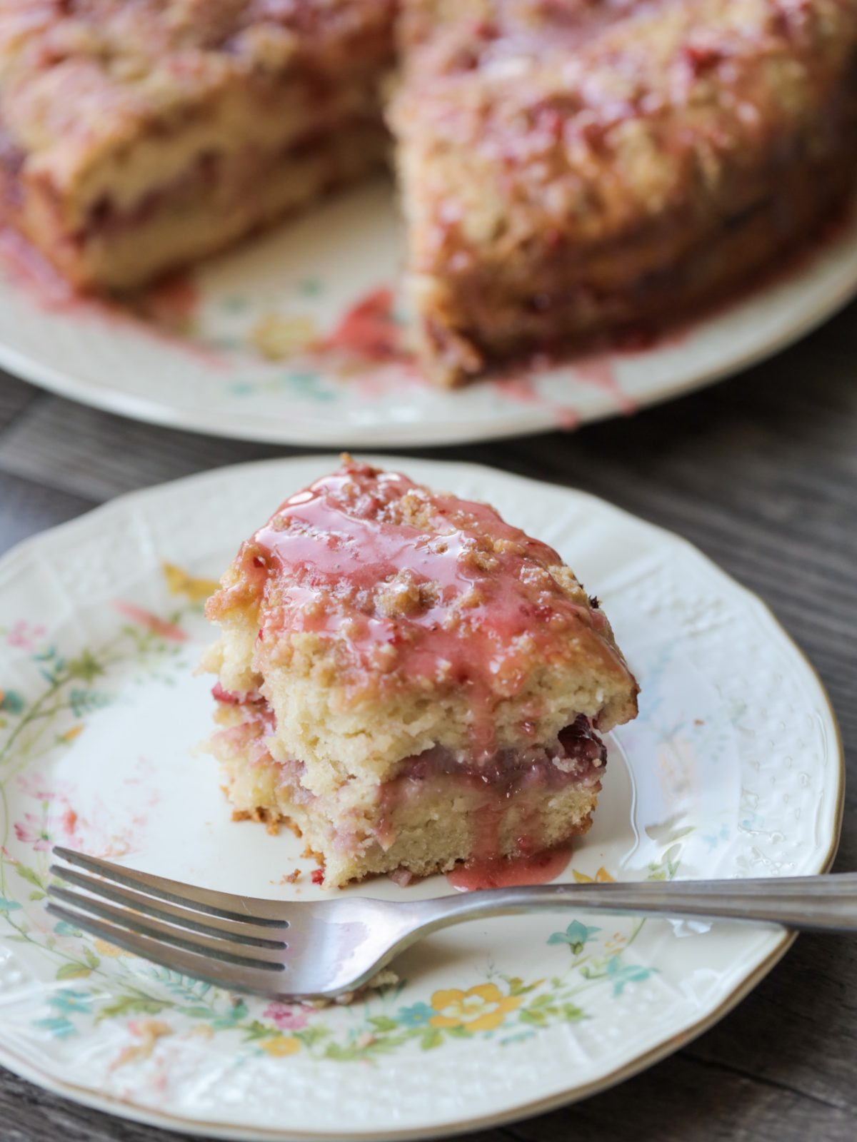 A half eaten strawberry sourdough discard coffee cake sits on a floral plate with the full sourdough coffee cake in the back.