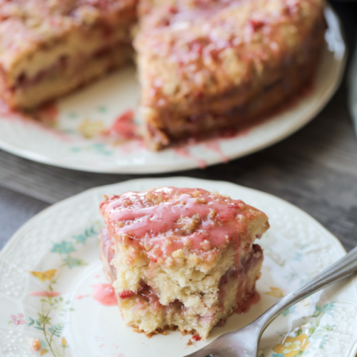 A half eaten slice of strawberry sourdough discard coffee cake sits on a floral plate. The rest of the cake sits in the background.