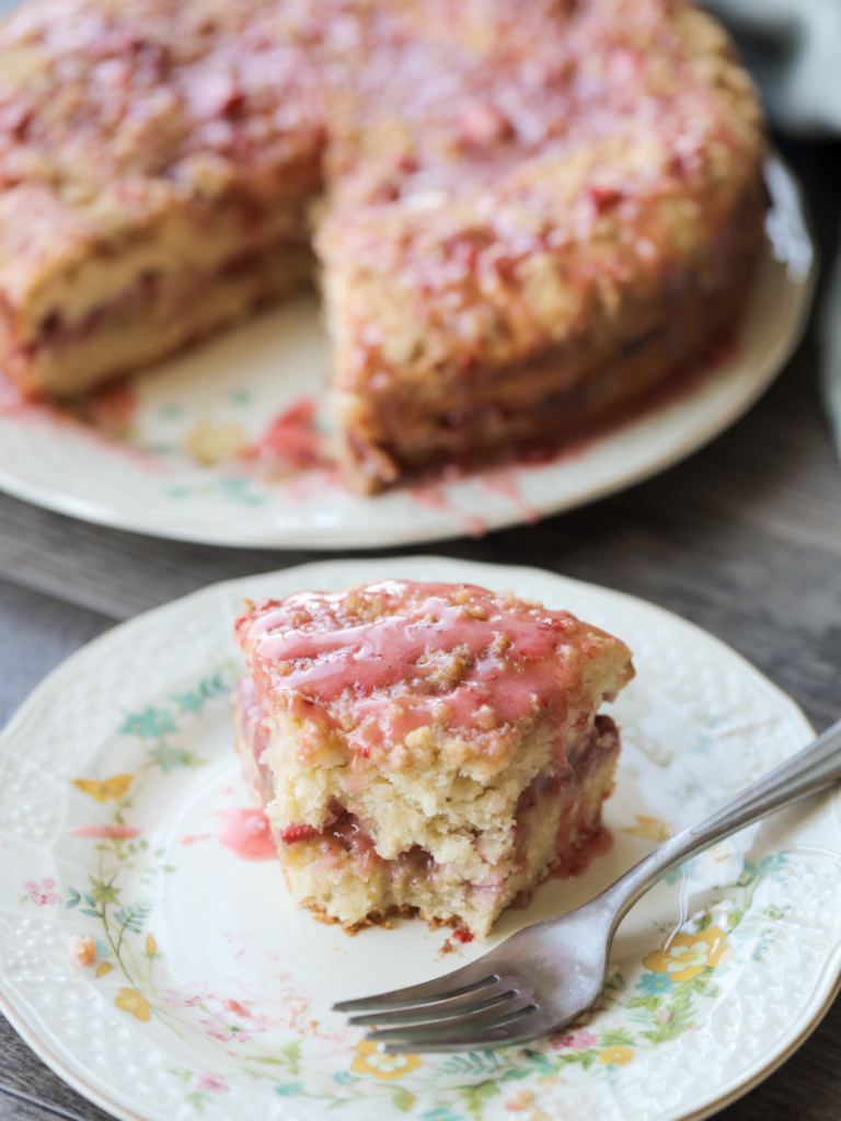 A half eaten slice of strawberry sourdough discard coffee cake sits on a floral plate. The rest of the cake sits in the background.