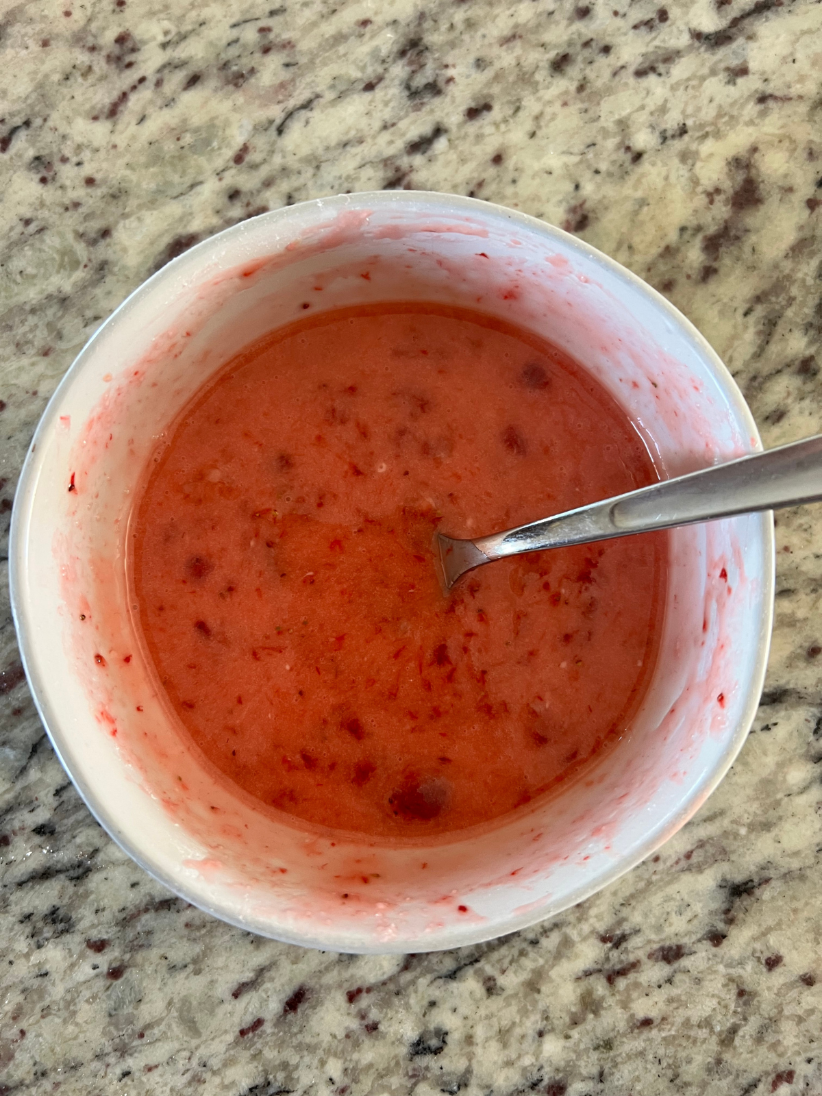 The strawberry icing sits in a bowl with a spoon in it.