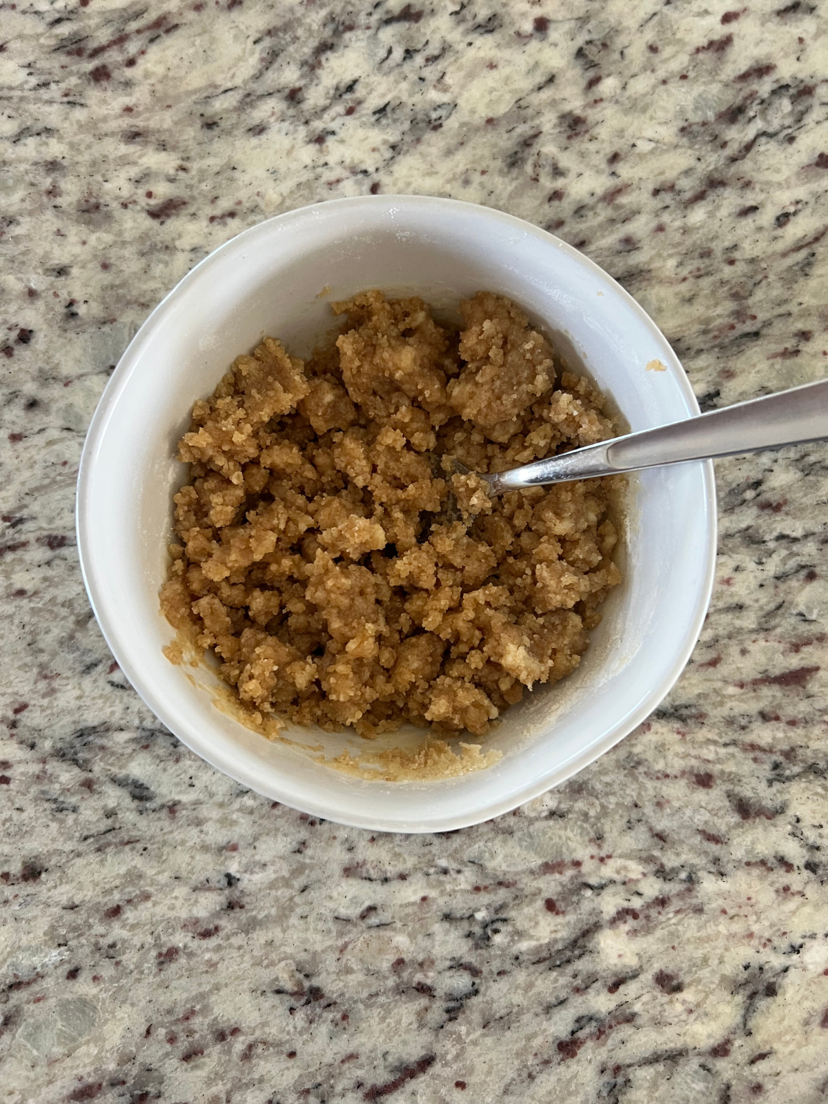 A white bowl contains the streusel for this sourdough strawberry coffee cake recipe. A fork sits in the bowl. 