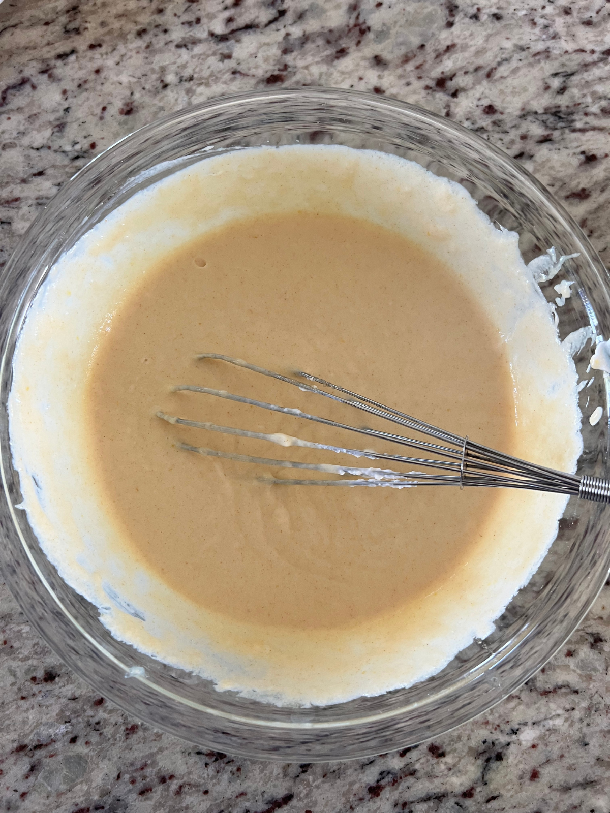 The wet ingredients for the sourdough strawberry coffee cake are shown in a glass bowl with a whisk.