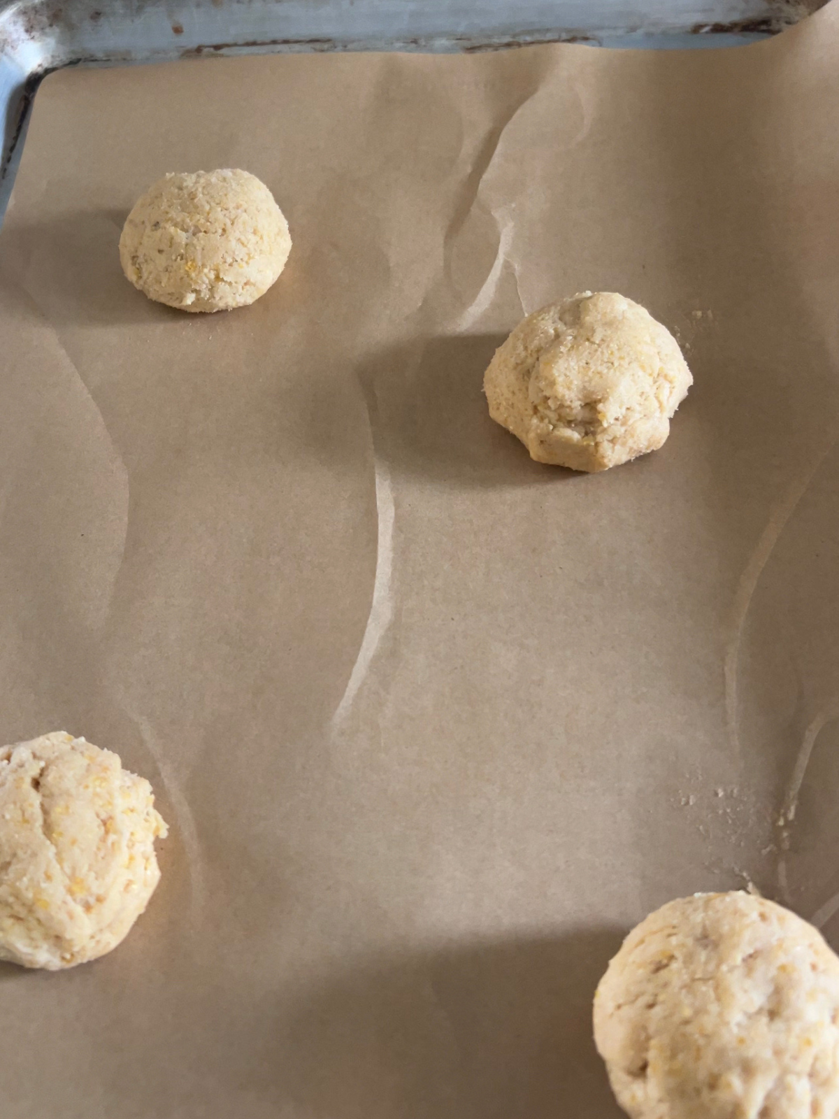 The sourdough cornbread cookie dough balls sit on a parchment paper-lined baking sheet.