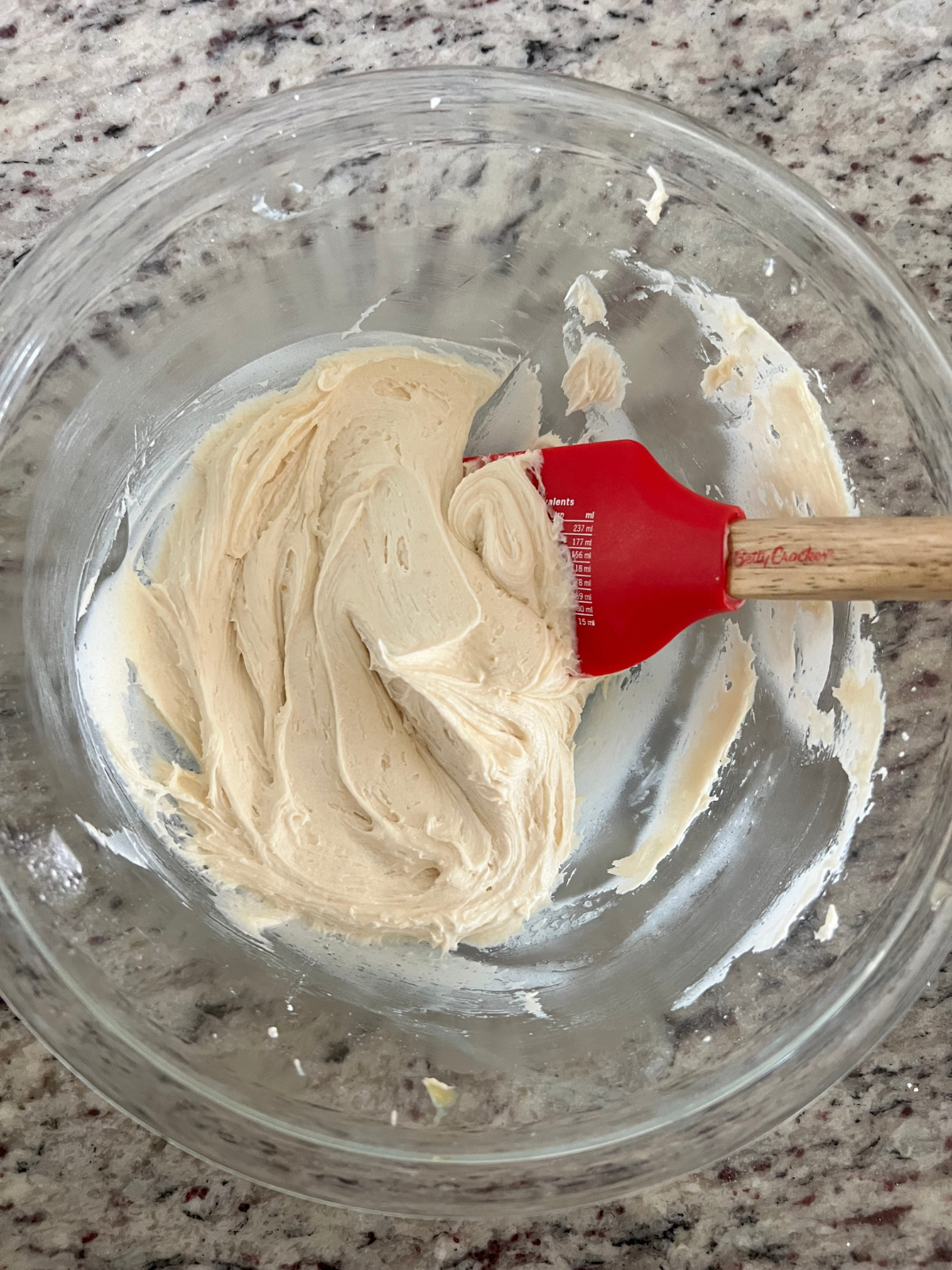 The honey buttercream frosting sits in a glass mixing bowl with a rubber spatula in it.