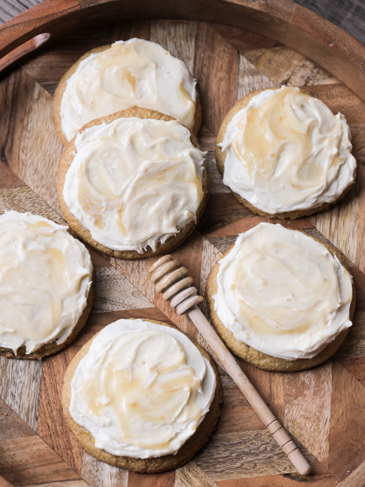 Several sourdough cornbread brown butter cookies with honey buttercream frosting sit on a wooden serving platter.