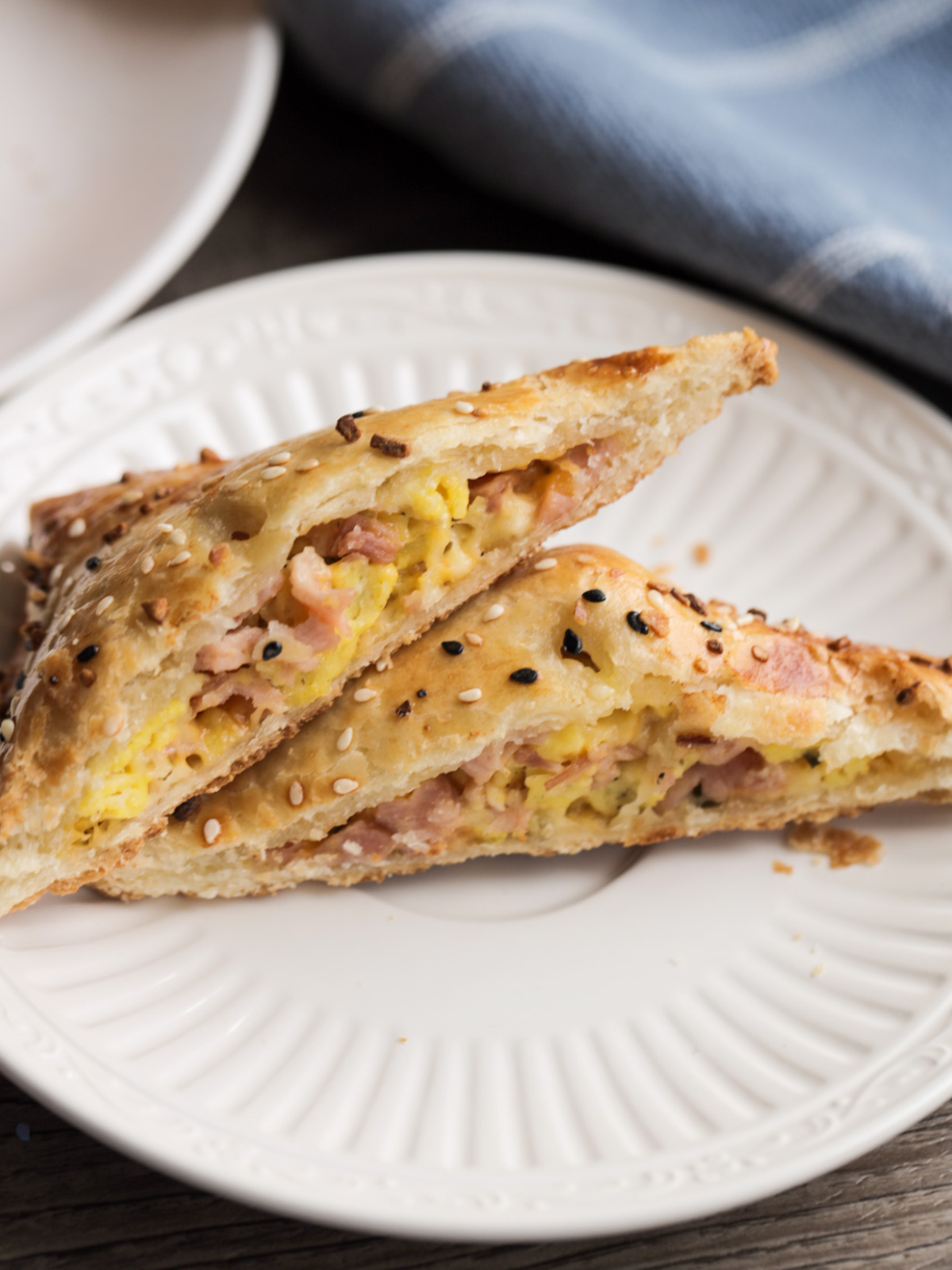 A closeup of a sourdough discard hand pie with cheese, ham, and eggs are shown cut in half. The smoked gouda and cheddar are gooey and you see the everything bagel seasoning on the tops of the golden crusts.