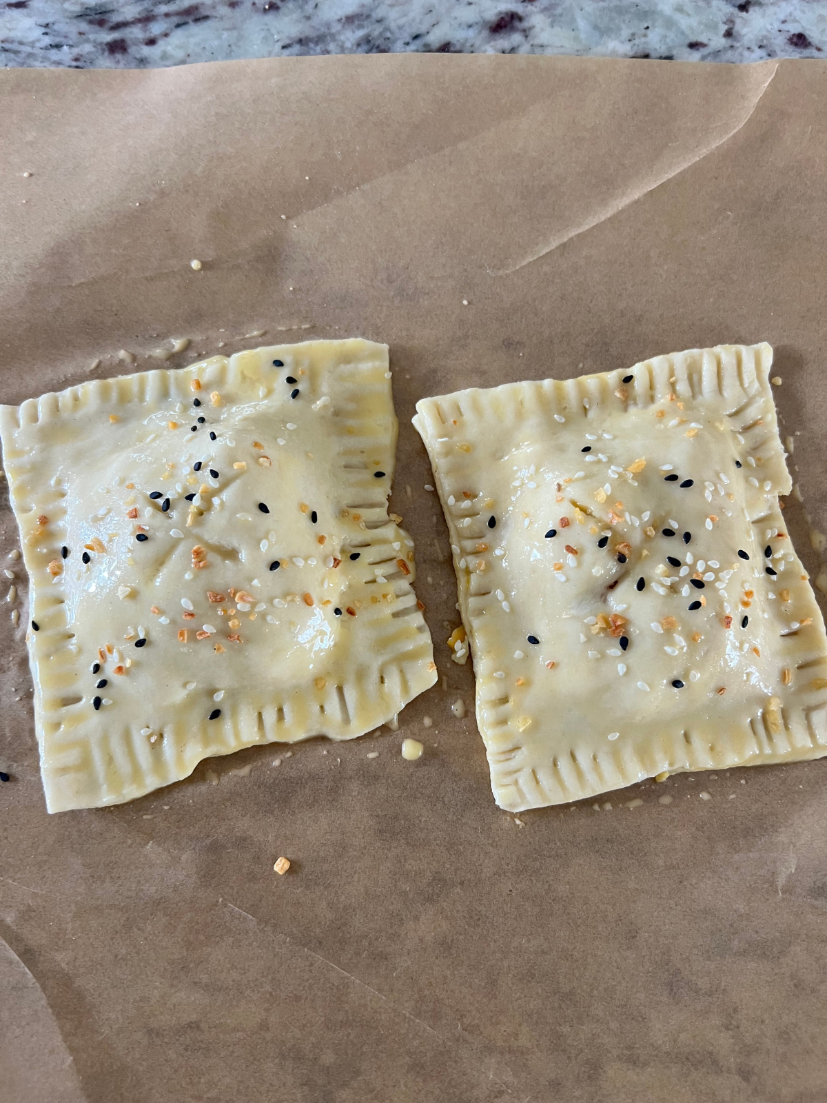 The sourdough discard ham, cheese, and egg hand pies are shown unbaked with the egg wash brushed over them and the everything bagel seasoning sprinkled over them.