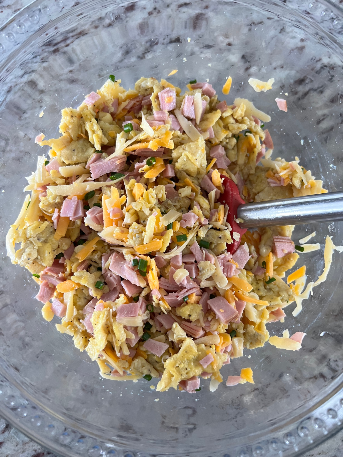 The filling for the sourdough cheesy egg and ham hand pies are shown in a glass mixing bowl. 