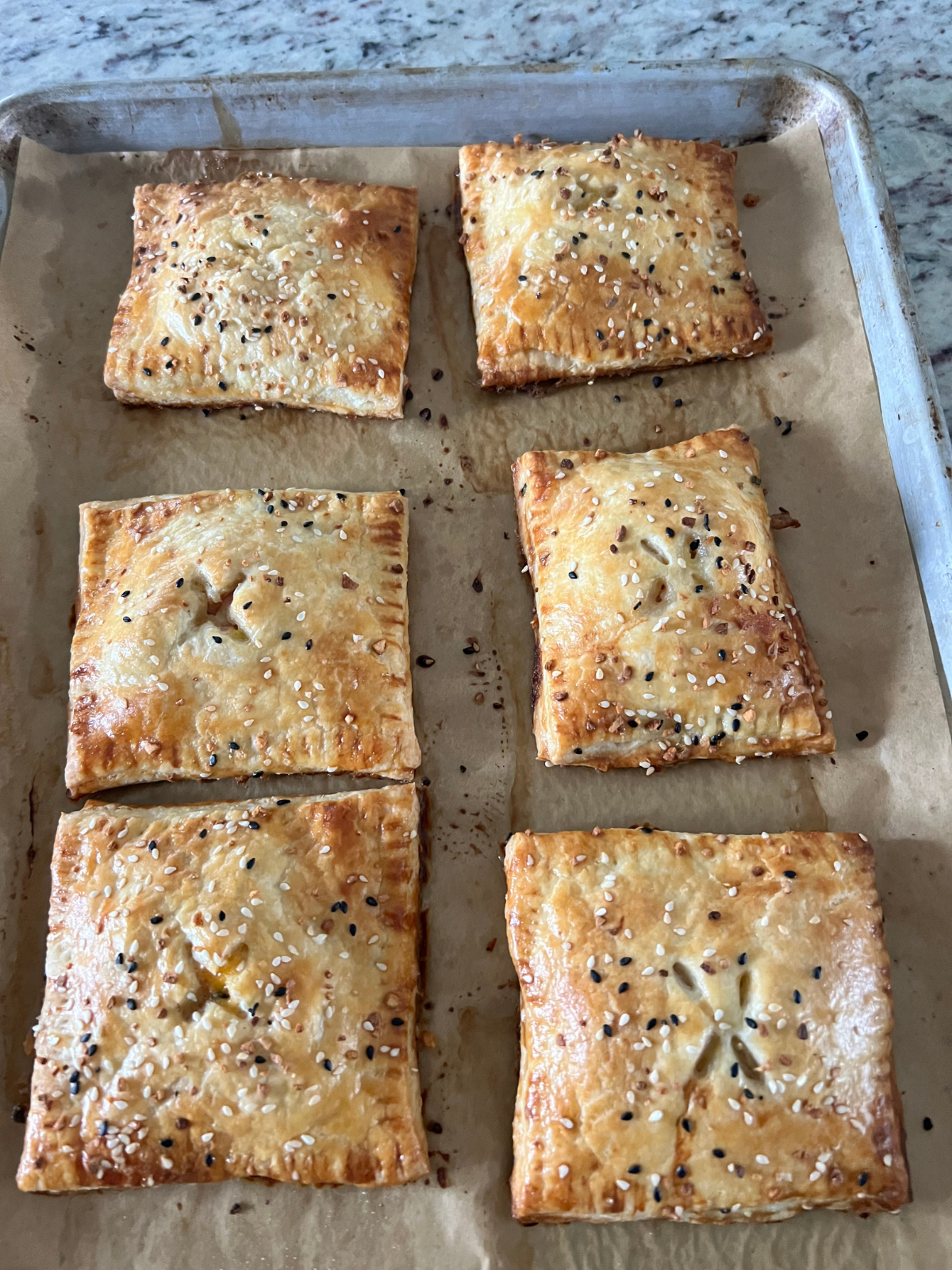 The sourdough discard ham, cheese, and egg hand pies are shown freshly baked on a parchment paper-lined baking sheet.