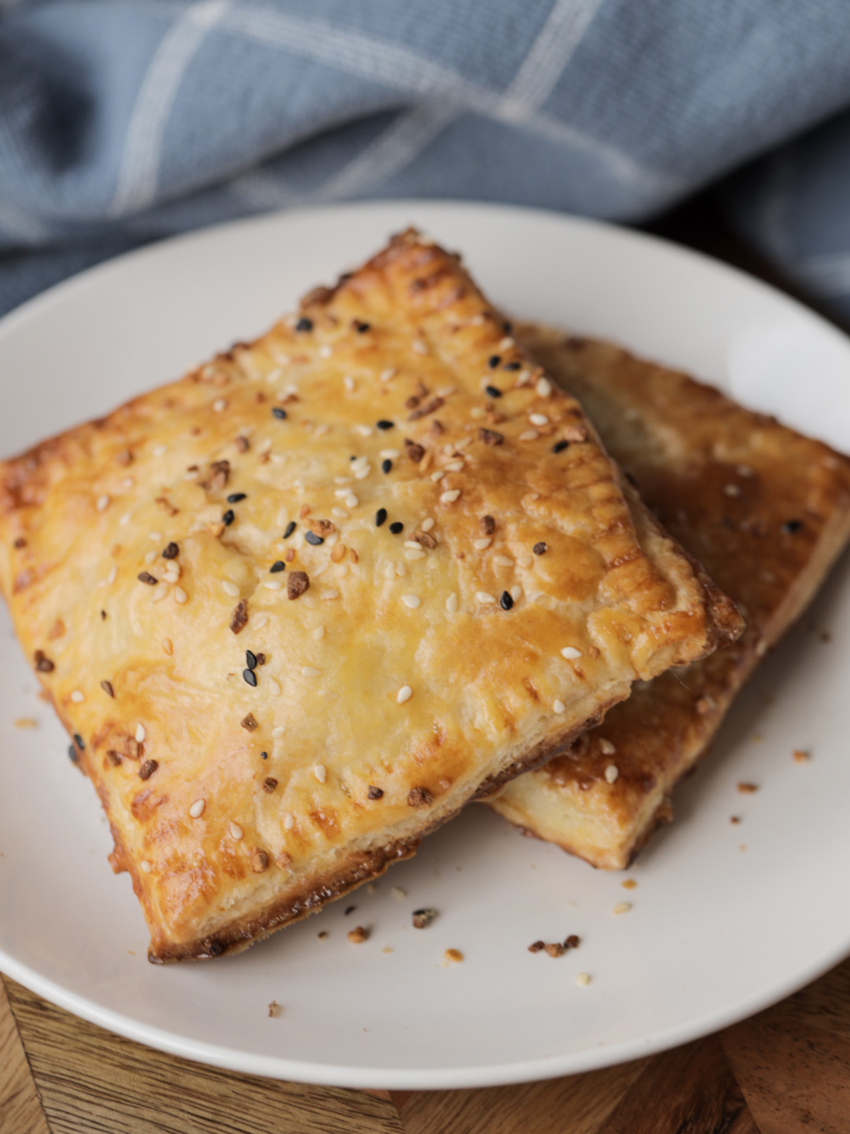 Two cheesy ham & egg sourdough discard hand pies sit on a plate. They are golden brown and topped with everything bagel seasoning.