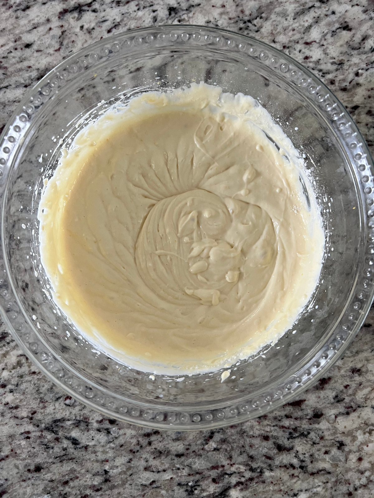 The lemon cheesecake filling sits in a glass mixing bowl after being mixed together.
