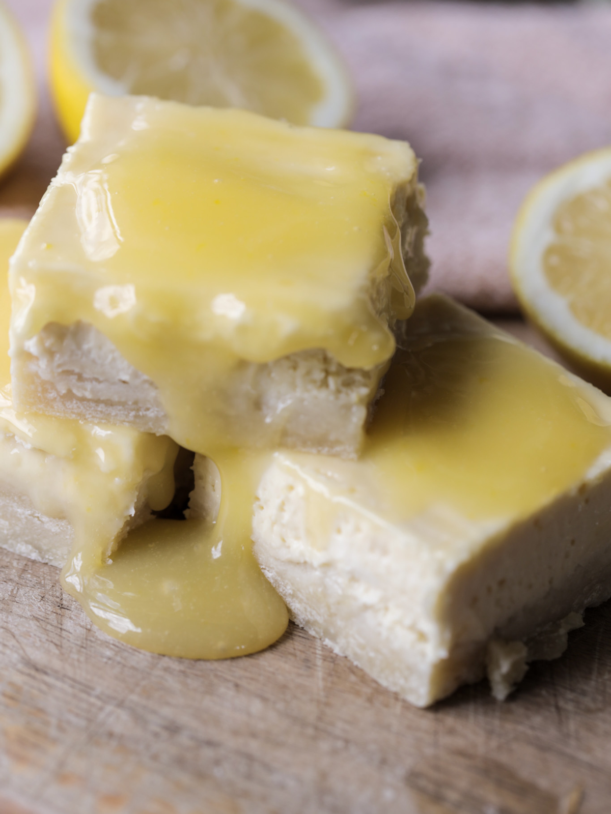 Three lemon curd cheesecake bars with sourdough discard shortbread crust sit stacked on each other. Lemon curd drips in the most delicious way down these cheesecake bars!