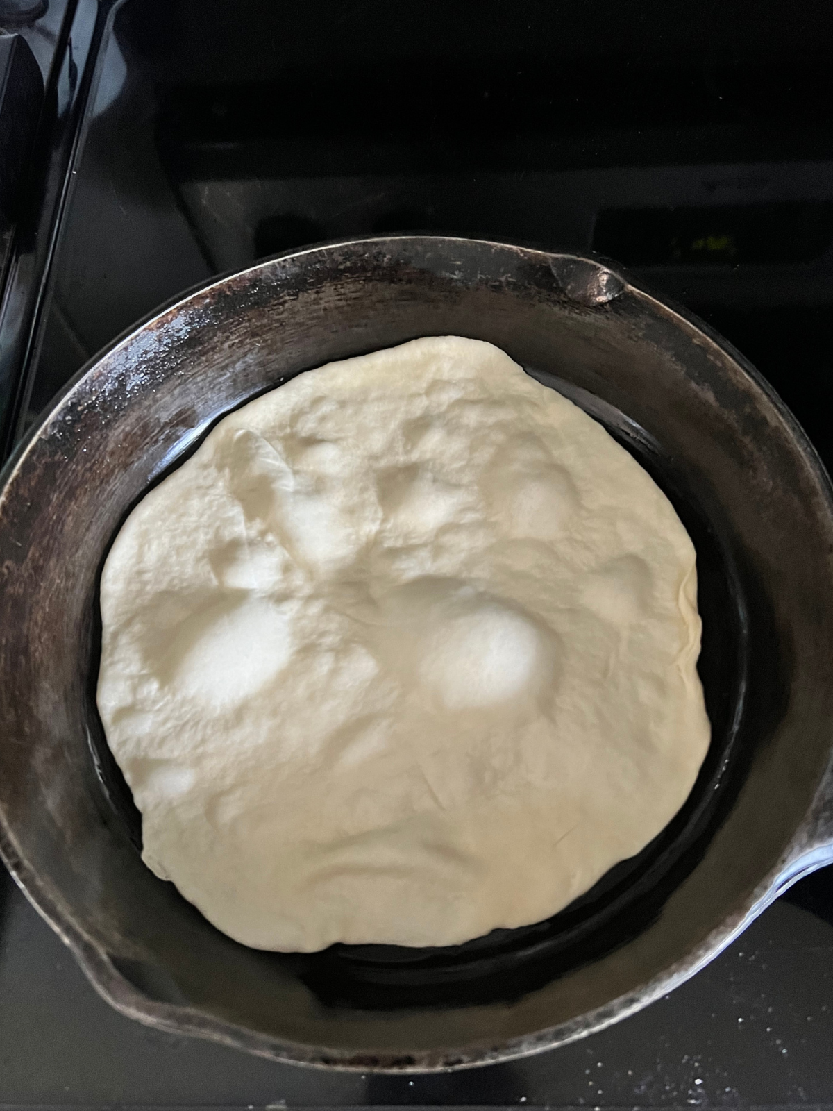 The sourdough discard tortilla is shown cooking on a cast-iron skillet while the uncooked side shows bubbles. 